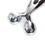 Rodillo facial y corporal 3D plateado con doble esfera facetada y mango brillante.