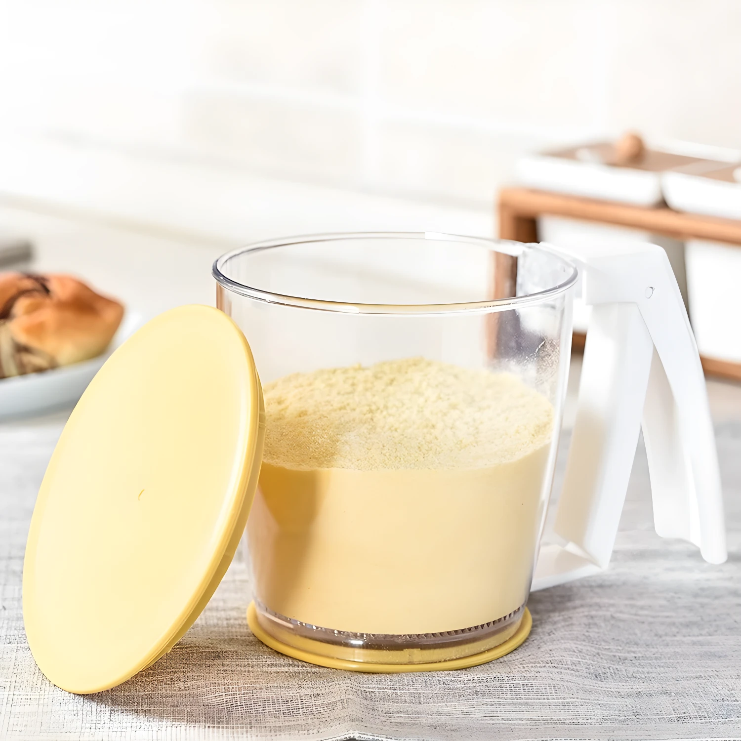Tamiz dispensador manual para harina con tapa amarilla y asa blanca en cocina.