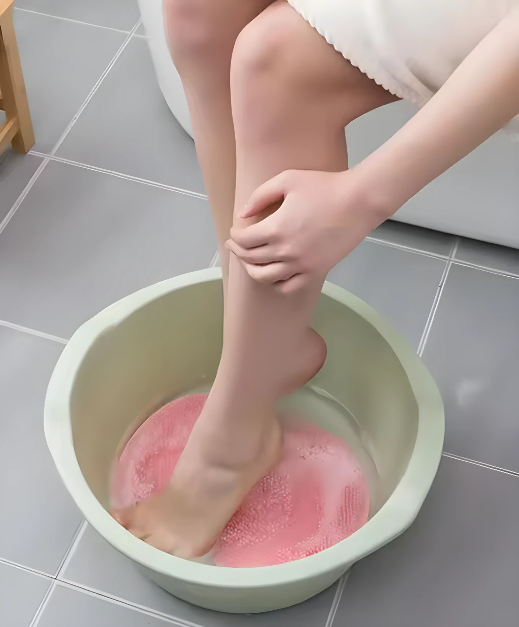 Mujer sumerge pie en tina de baño con tapete antideslizante rosa para masaje.