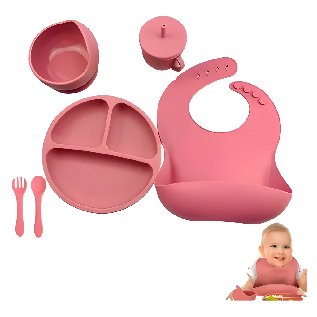 Vajilla de silicona para bebé: plato dividido, cuenco, vaso, cubiertos y babero rosados.