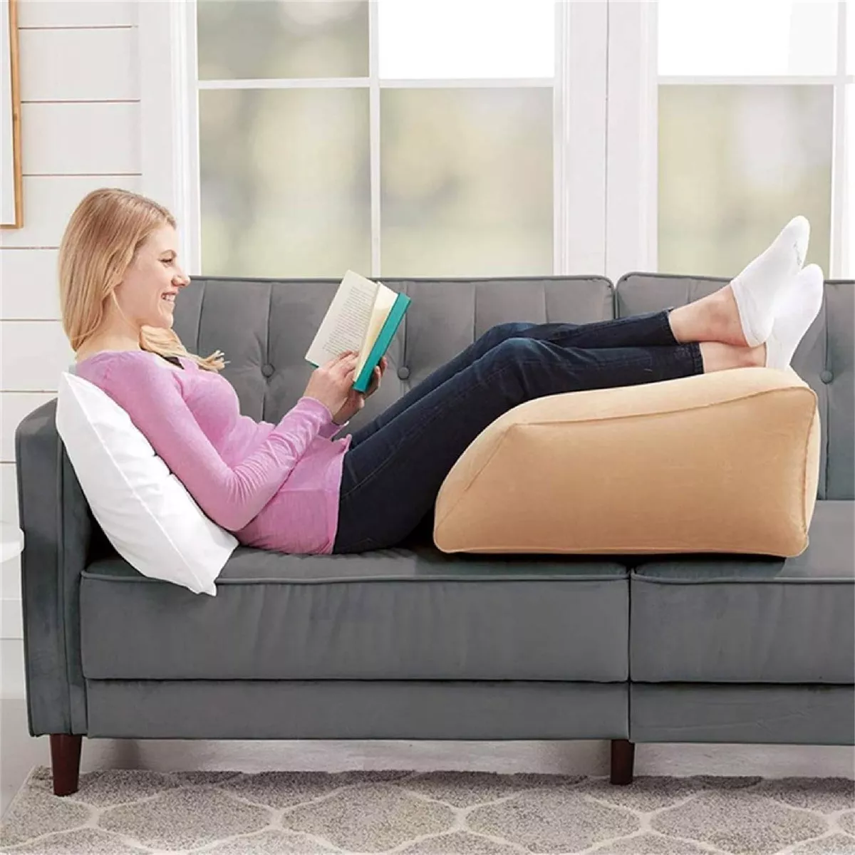Mujer lee libro en sofá con almohada inflable color camel para elevar piernas.