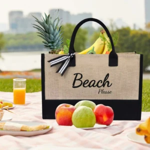 Bolso de yute color natural y negro para playa con texto "Beach Please", lleno de frutas.