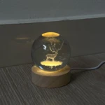Lámpara esfera de cristal 3D con ciervo iluminado sobre base de madera.