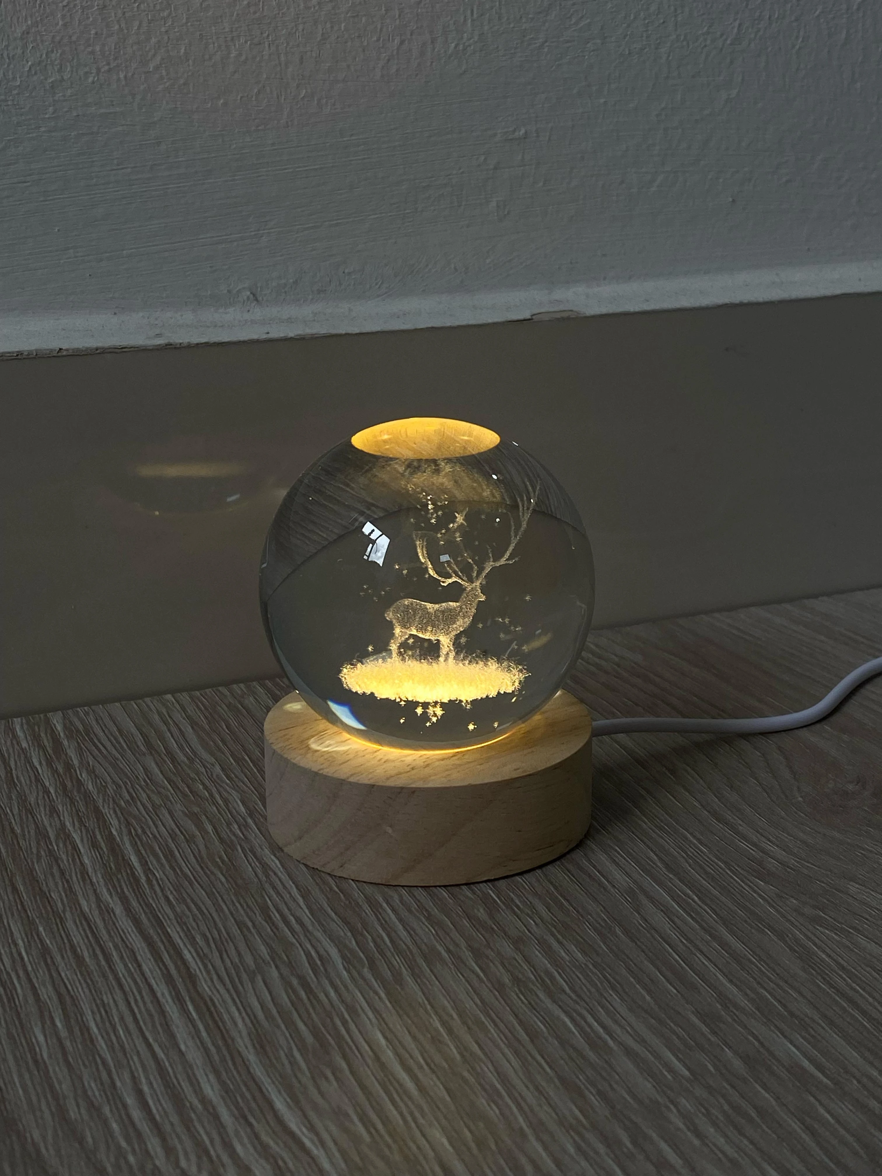 Lámpara esfera de cristal 3D con ciervo iluminado sobre base de madera.