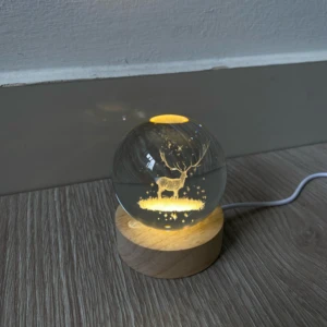 Lámpara esfera de cristal 3D con reno grabado, luz cálida, base de madera.