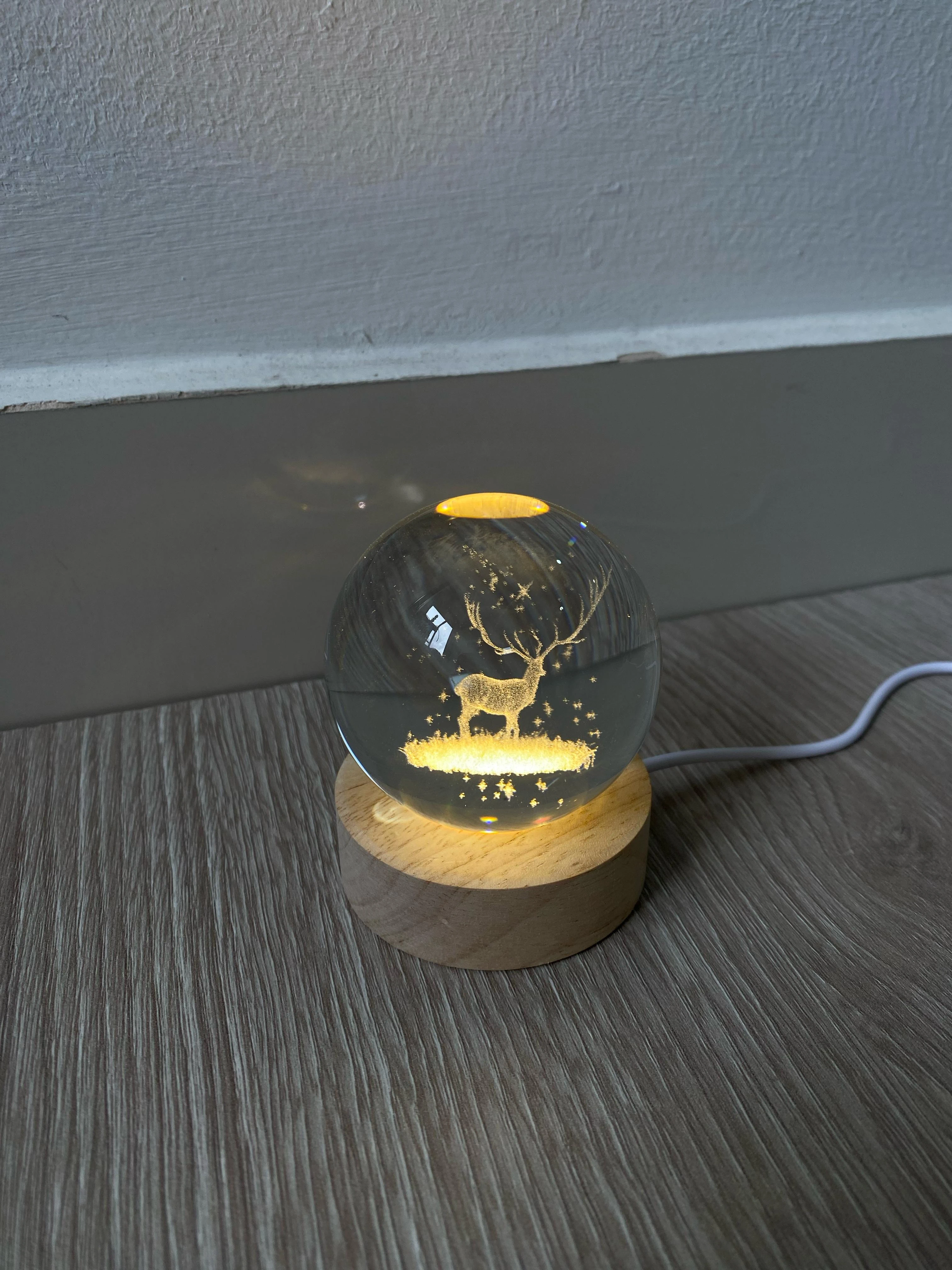 Lámpara esfera de cristal 3D con reno grabado, luz cálida, base de madera.