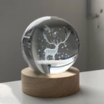 Esfera de cristal 3D grabada con ciervo y estrellas sobre base de madera.