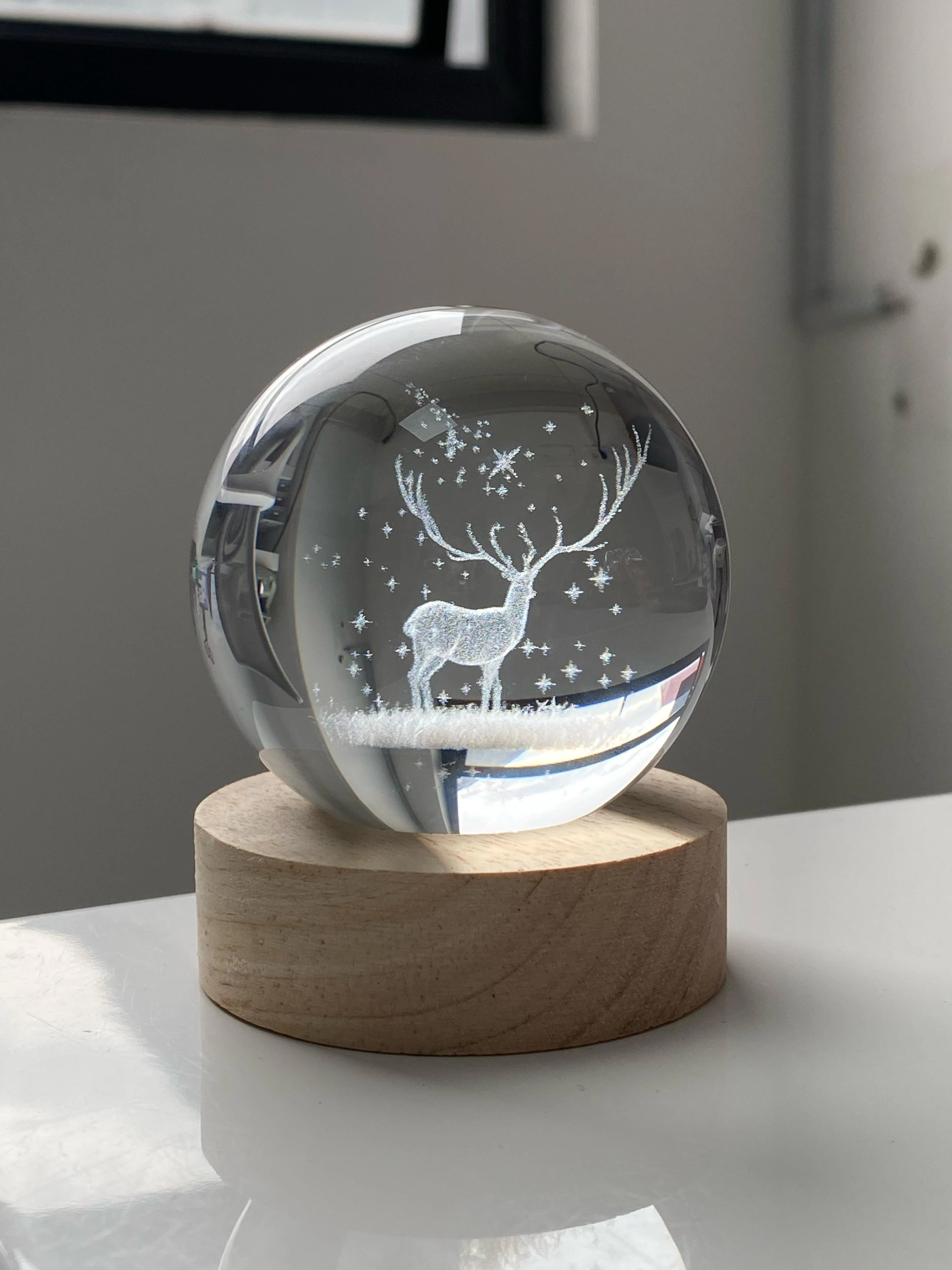 Esfera de cristal 3D grabada con ciervo y estrellas sobre base de madera.