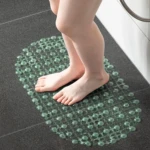 Tapete de baño transparente texturizado con ventosas, con pies sobre él, en suelo de baño oscuro.