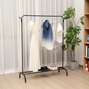 Perchero minimal negro con ropa colgada y zapatos en la base, junto a planta y estantería.