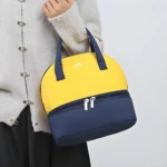 Bolso nevera para leche materna amarillo y azul marino de dos compartimentos, sostenido por una persona.