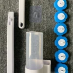 Cepillo limpiador de inodoro desechable: mango blanco, recipiente, cabezales azules tipo flor y adhesivo.