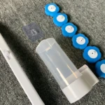 Cepillo limpiador de inodoro desechable con cabezales de repuesto azules y soporte transparente, sobre superficie gris.