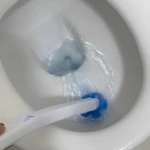 Cepillo desechable para inodoro, limpiando con agua azul en taza de cerámica blanca.