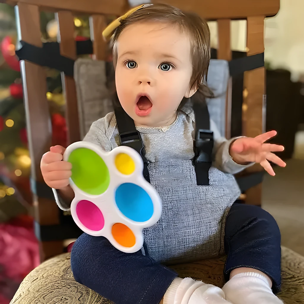 Niña sentada en silla con arnés, juega con sonajero de colores.