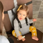 Niña en asiento con cinturón de seguridad gris y pantalón estampado de gatos amarillos.