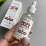 Sérum facial Arbutin White Sadoer con Nicotinamida, en frasco de vidrio transparente con gotero, enfocado en piel blanca.
