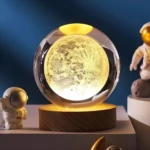 Lámpara de escritorio 3D con esfera de luna en cristal y base de madera, acompaña un astronauta.