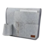 Organizador de cama de fieltro gris con compartimentos para tablet, gafas y control remoto.