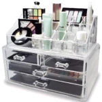 Organizador acrílico transparente con cajones y compartimentos para maquillaje, incluyendo paletas y tubos.