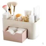 Organizador de maquillaje beige con cajón rosa, compartimentos para brochas y cosméticos, y almohadillas de algodón.