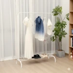 Perchero minimal blanco con ropa colgada, plantas y estanterías al fondo.