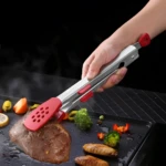 Pinzas de acero inoxidable con puntas rojas perforadas para cocinar carne y vegetales en parrilla.