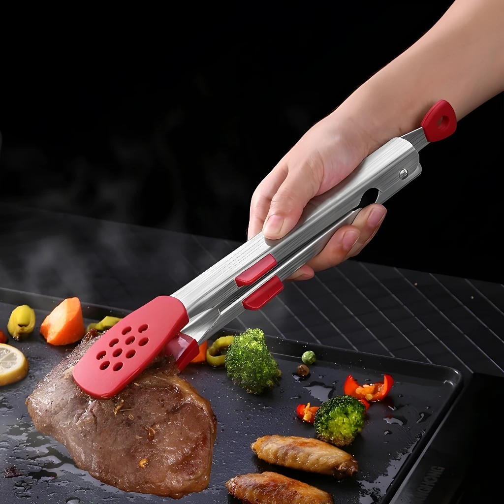 Pinzas de acero inoxidable con puntas rojas perforadas para cocinar carne y vegetales en parrilla.