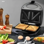 Sanduchera eléctrica doble con dos sándwiches dorados y crujientes, ingredientes frescos y molinillos de madera.