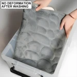 Tapete de baño gris con textura de piedras suaves, sin deformación tras lavado, dentro de caja plástica.