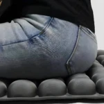 Tapete de silla gris con textura de burbujas, bajo persona usando jeans azules, para aliviar presión.