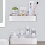 Estante adhesivo blanco con productos de baño: jabón líquido, loción, crema dental, cepillo y planta.