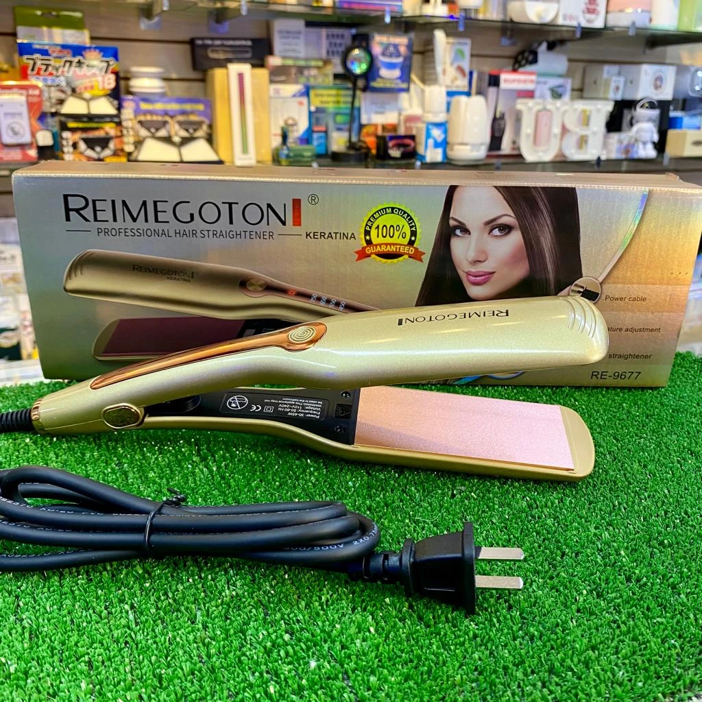 Plancha de cabello Reimegoton dorada con placas de cerámica rosa, sobre su caja original en un mostrador de tienda con césped artificial y cable de red.