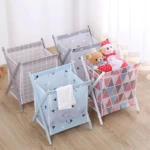 Cuatro canastas plegables para ropa y juguetes: cuadrícula gris, azul con triángulos, gris con triángulos y geométrica rosa, sobre piso de madera.