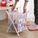 Canasta plegable de tela con soporte en X blanca y estampado geométrico rosa, azul y gris, usada para organizar.