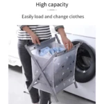 Canasta plegable gris con patrón geométrico de triángulos, llena de ropa, siendo vaciada en lavadora por una persona.