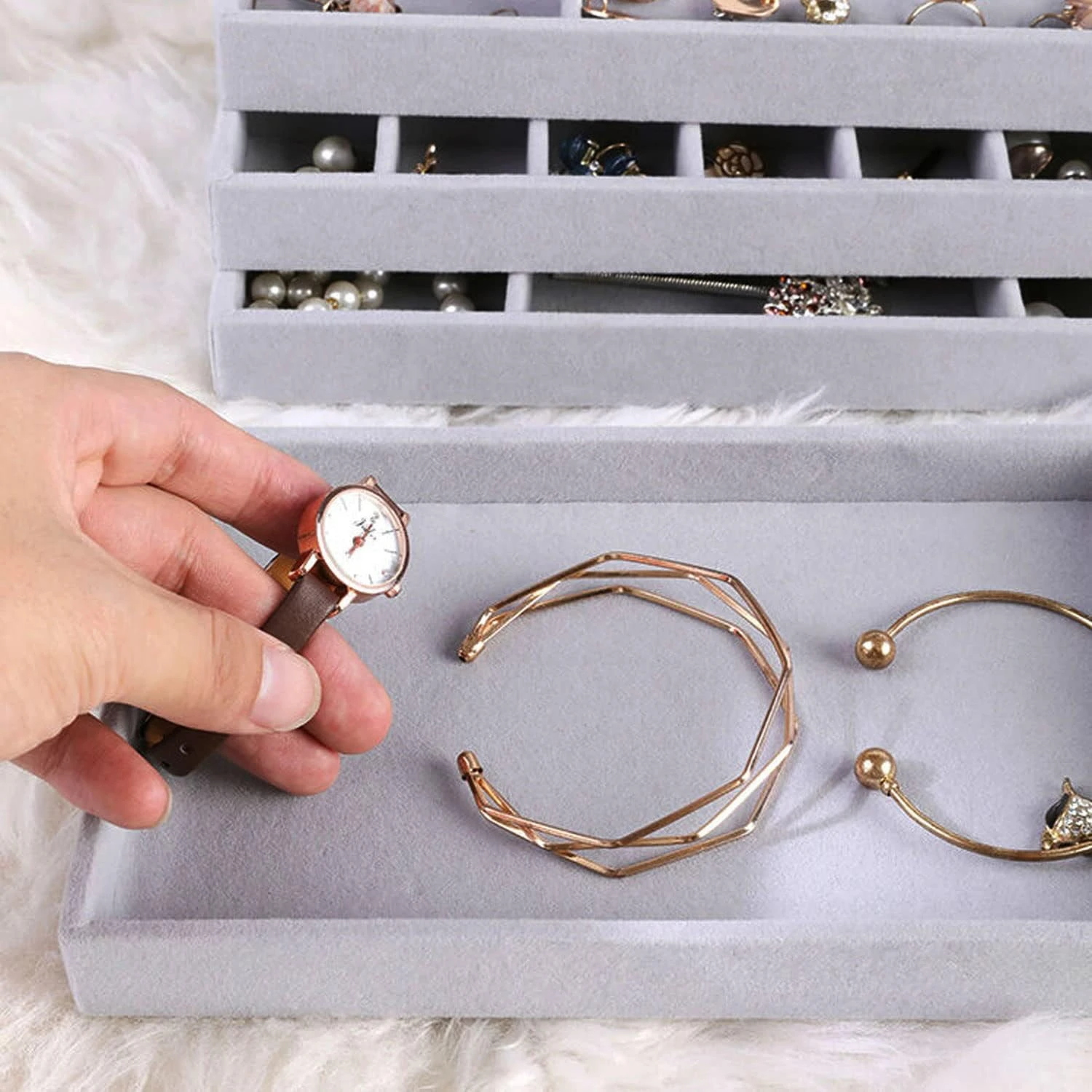 Organizador de joyas de terciopelo gris con compartimentos, mostrando un reloj, pulseras y joyas.