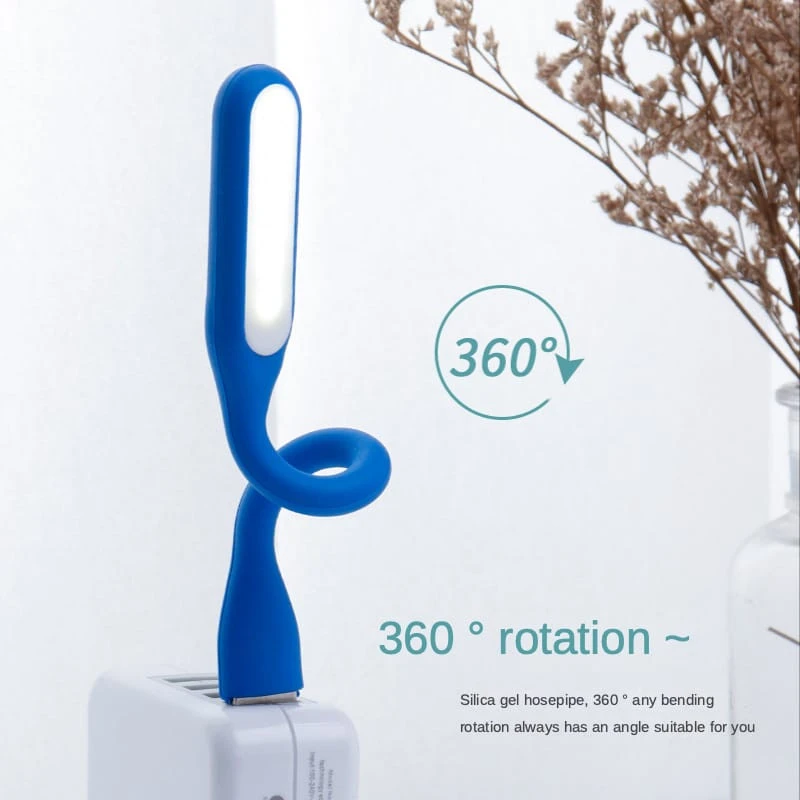 Mini lámpara LED azul con cuello flexible de silicona que permite una rotación de 360 grados, conectada a un cargador USB sobre una superficie blanca.