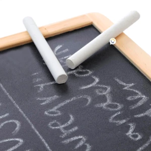 Pizarra didáctica con dos tizas blancas apoyadas, letras escritas con tiza sobre superficie negra.