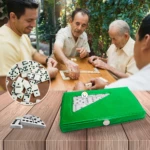 Caja verde de dominó para juego de mesa, con fichas visibles, sobre mesa de madera.