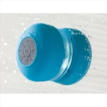 Altavoz azul recargable para ducha con botones de control, salpicado de agua.