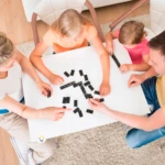 Familia jugando dominó de madera sobre mesa blanca.
