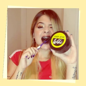 Mujer sonriente usa cepillo y carbón activado Wiki para blanquear dientes.