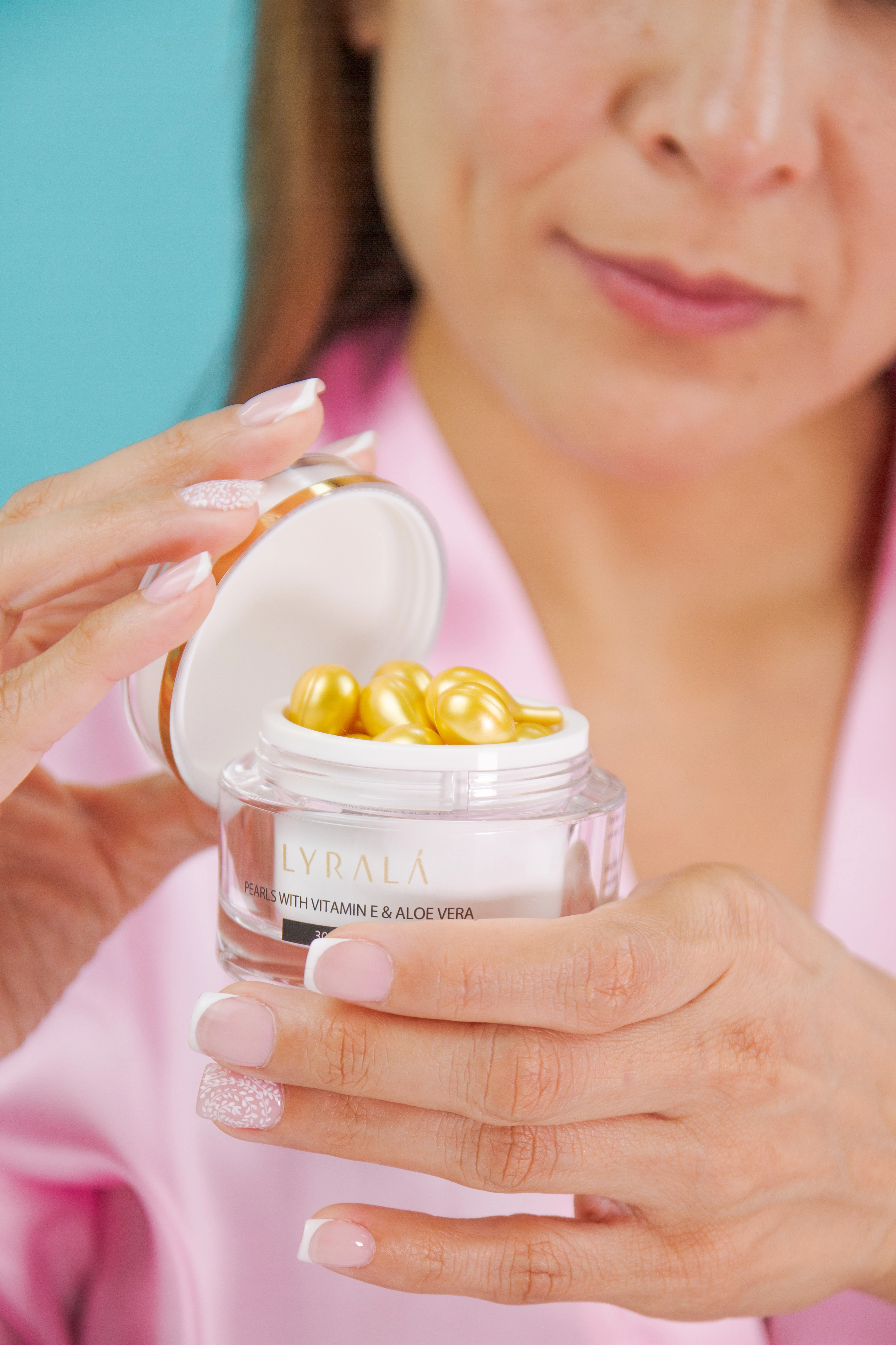 Manos sostienen frasco de Lyralá con perlas doradas de sérum, fondo azul y ropa rosa.