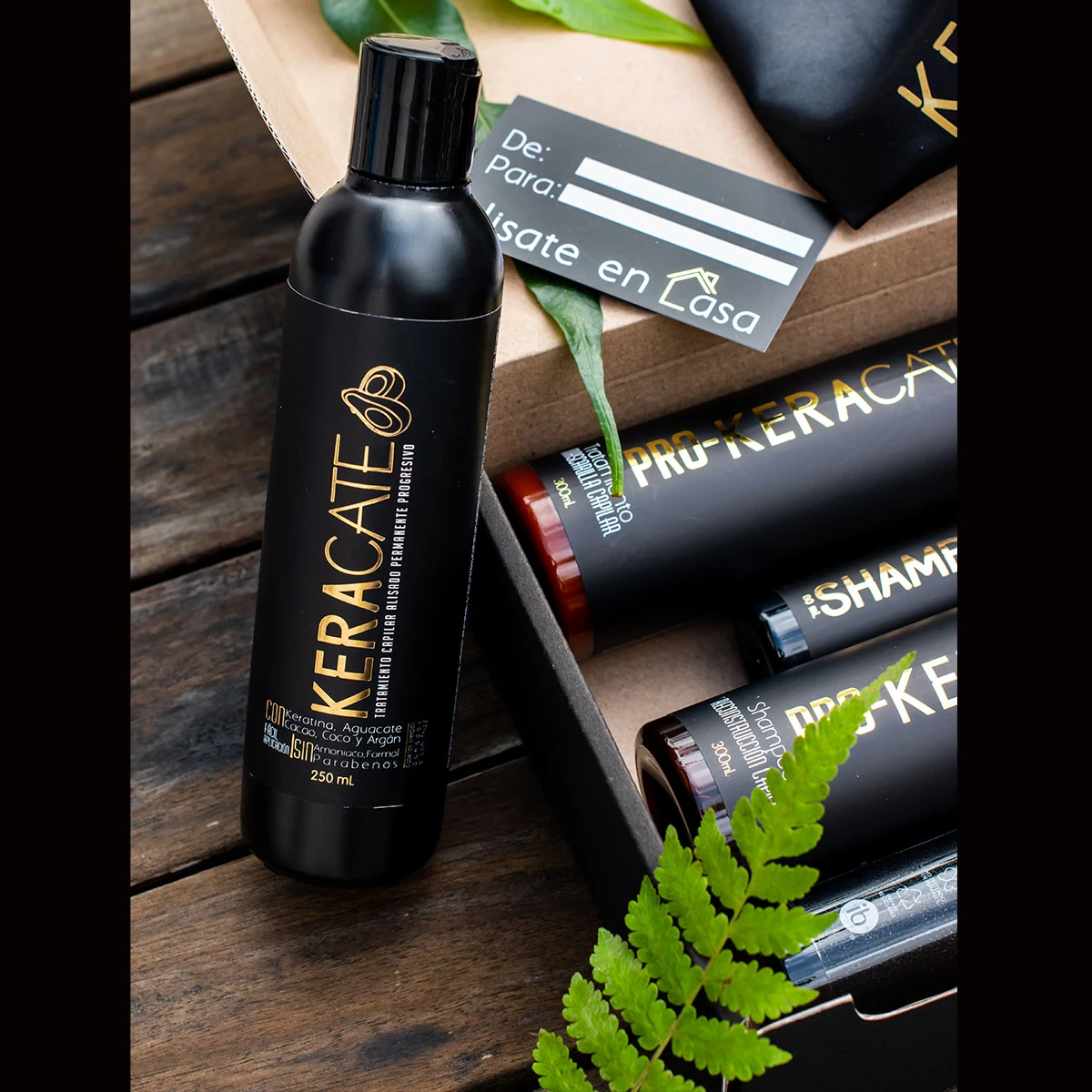 Set de tratamiento capilar Keracate con alisante progresivo de 250ml, shampoo y productos de cuidado en caja negra sobre superficie de madera con helecho.