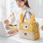Lonchera térmica amarilla con diseño de conejo, asas grises, ideal para llevar comida.