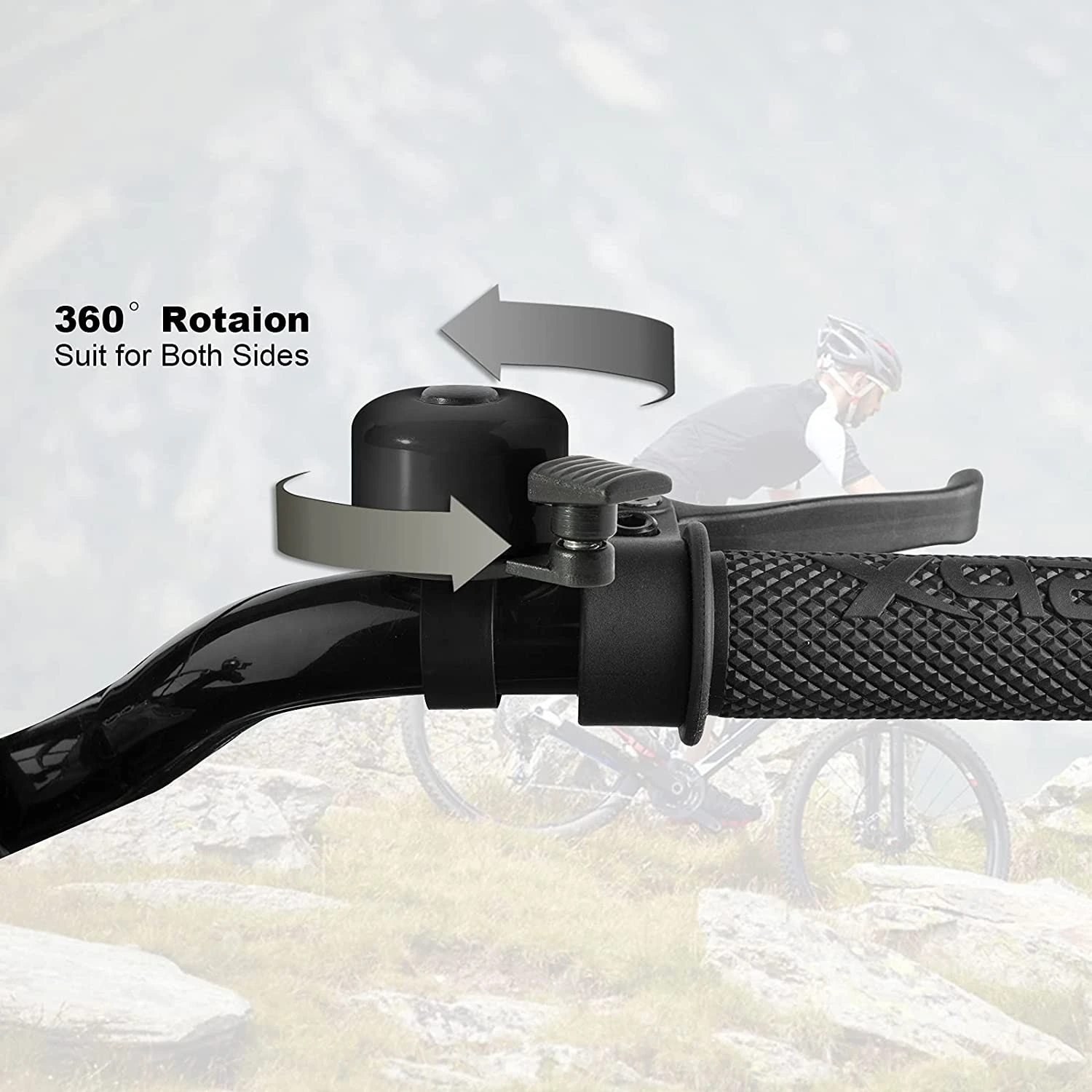 Timbre negro para bicicleta con rotación 360°, montado en manubrio junto a freno, fondo desenfocado de ciclista en montaña.