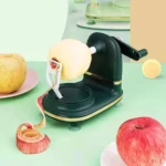 Picador de manzanas verde oscuro con manivela, pelando una manzana amarilla en una superficie verde.