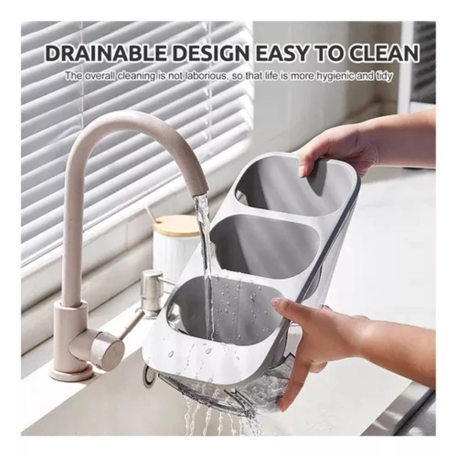 Organizador de cubiertos de tres compartimentos en color gris, siendo lavado bajo el grifo de la cocina para mostrar su diseño drenable.