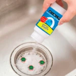 Persona vaciando polvo "Bubble Bombs" en un desagüe de lavabo con tres caricaturas de bacterias.
